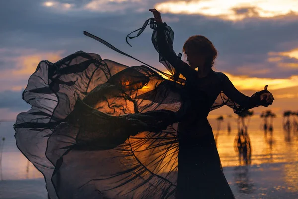 Jovem mulher em pé na água ao pôr do sol silhueta — Fotografia de Stock