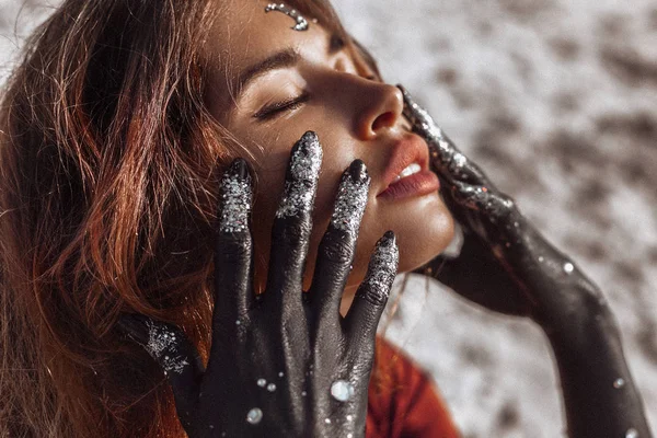 Close up de bela jovem mulher com as mãos pintadas de preto . — Fotografia de Stock