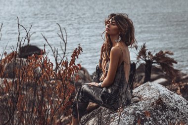 denizde taş üzerinde oturan güzel genç boho tarzı kadın 
