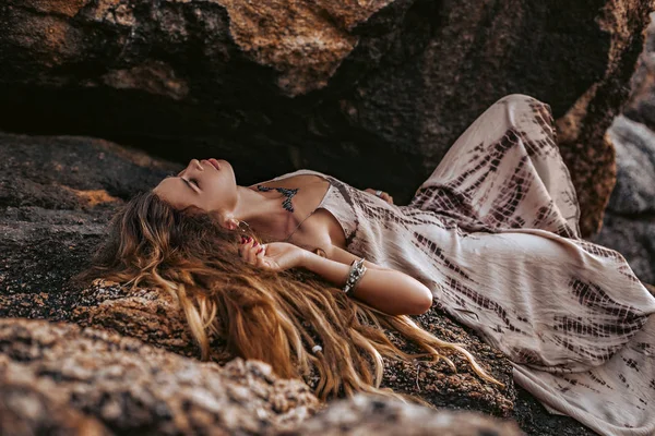 Bella giovane donna boho stile sdraiato su pietre al tramonto — Foto Stock