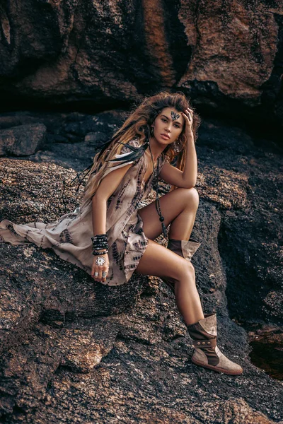 Bela jovem boho mulher estilo sentado em pedras ao pôr do sol — Fotografia de Stock