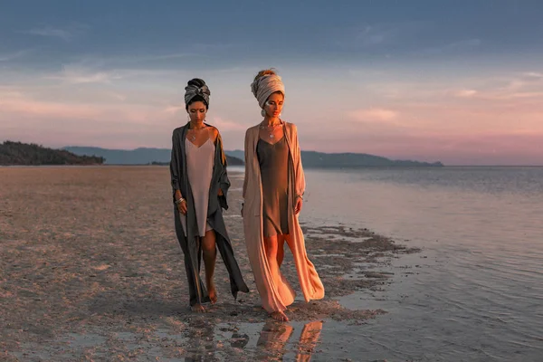 Twee jonge mooie meisjes in tulband wandelen op het strand — Stockfoto