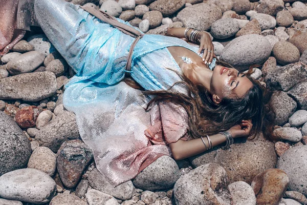 Beautiful young woman in elegant dress lying on stone beach — 图库照片