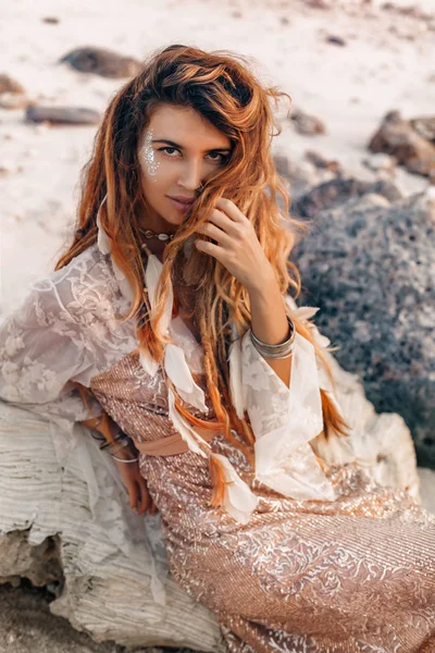 Jonge modieuze vrouw zittend op het stenen strand portret — Stockfoto