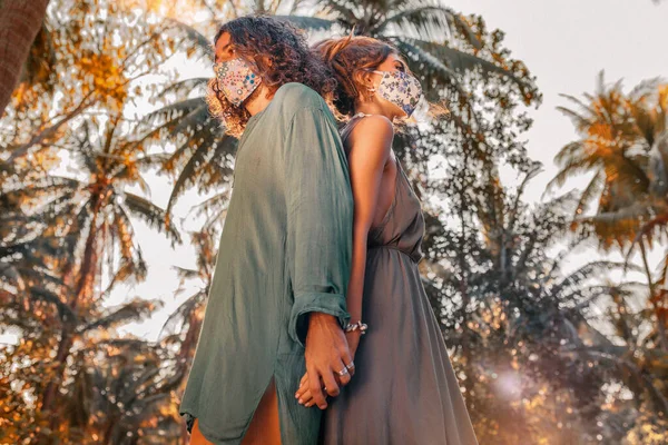 医療用のマスクと手袋をした美しい若いカップルが日没時に屋外に立ち ロイヤリティフリーのストック画像