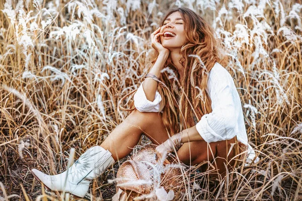 Sahada kovboy çizmeleri giyen güzel, genç ve neşeli bir kadın.