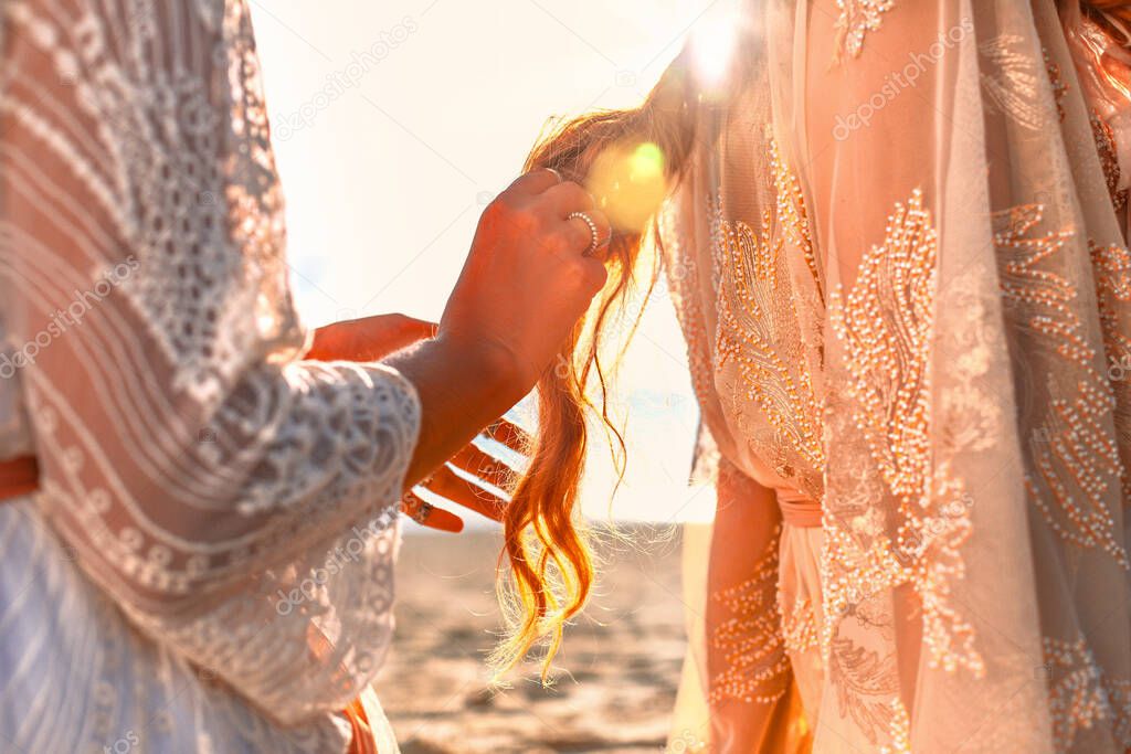 two beautiful young woman in elegant boho dresses oudoors at sunset