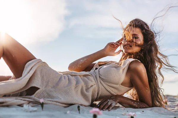 夕日のビーチで砂の上に寝そべっている美しい若い女性 — ストック写真