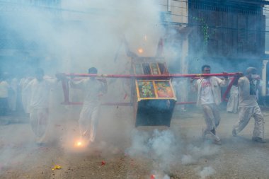 Phang Nga, Tayland - 14 Ekim 2018: Grup tahtırevan içinde sokakta yürüyen insanlar ibadet Tanrı Phang Nga, Tayland vejetaryen Festivali geçit havai fişek ateş ederken Çin Tanrı heykeli ile holding beyaz elbiseli adam
