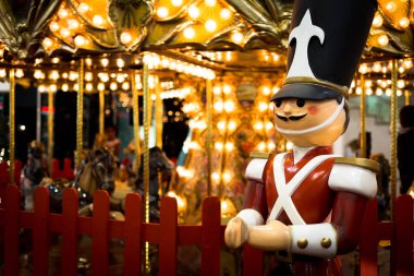Tin soldier in an amusement park with a moving carousel in the background clipart