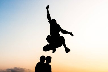 Genç kaykaycı kaykay ile iki erkek atlamak için çalışıyor