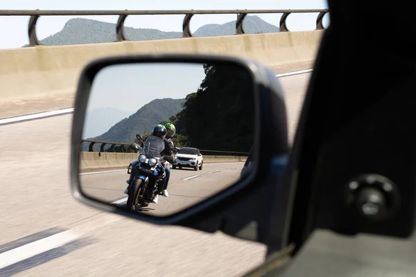 Car rear view mirror with the image of a biker approaching to overtake.