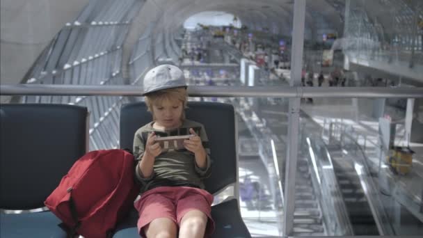 Bonito criança jogando jogos, assistindo filme no telefone inteligente no aeroporto — Vídeo de Stock