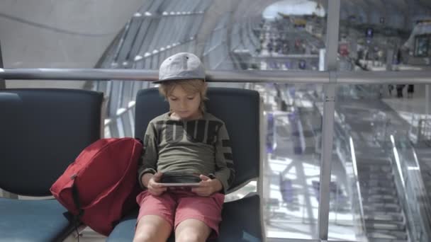 Lindo niño jugando juegos, viendo la película en el teléfono inteligente en el aeropuerto — Vídeos de Stock