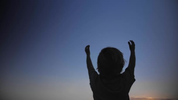 Criança silhueta levantando as mãos no ar no fundo do céu azul — Vídeo de Stock