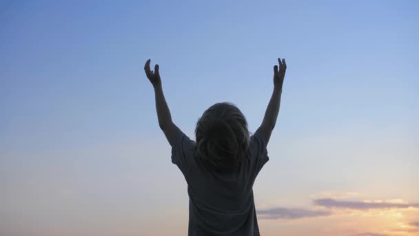 Kindersilhouette hebt die Hände in die Luft auf blauem Himmel Hintergrund — Stockvideo