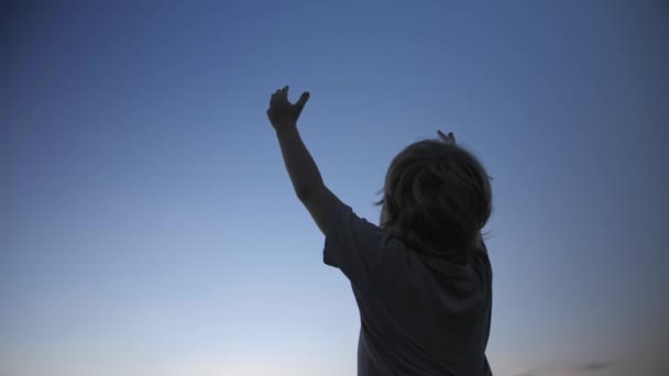 Barn siluett höjer händerna upp i luften på blå himmel bakgrund — Stockvideo