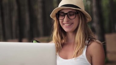 Gülümseyen kız yaz tatilinde dizüstü bilgisayar açık havada çalışıyor.