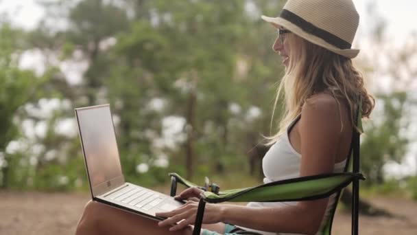 Glimlachend meisje werkt op laptop buitenshuis in zomer vakantie. — Stockvideo