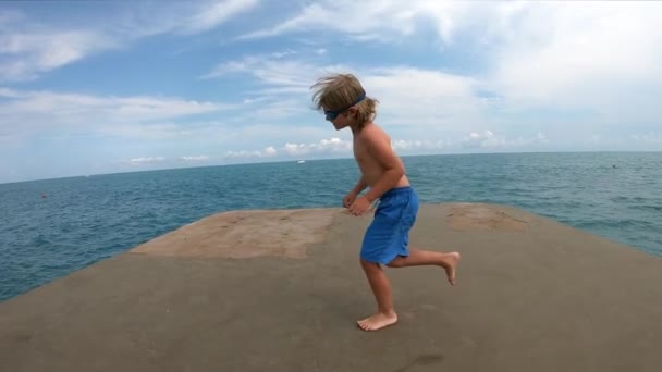 Criança correndo e pulando do cais na água do mar . — Vídeo de Stock
