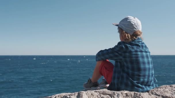 Gyermek ül a hegy tetején, és nézi a tengeri hullámok — Stock videók