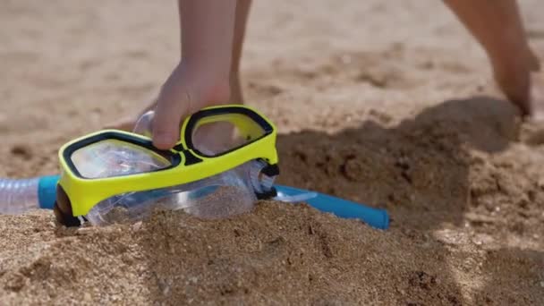 Крупним планом дитяча рука бере снорк, маску для дайвінгу на піщаному пляжі, щоб зануритися в море . — стокове відео