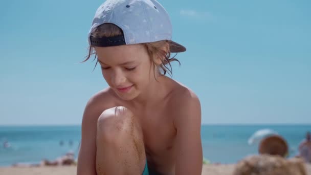 Portait di ragazzo sorridente che gioca con la sabbia sulla spiaggia su sfondo cielo blu — Video Stock