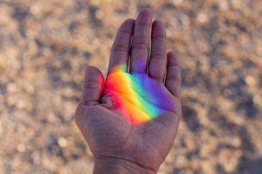 Üzerinde renkli gökkuşağı yansıması olan insan eli. Dışarıda gün batımı. Gurur günü konsepti. Lgbt aşk aşktır