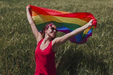 Açık havada yeşil bir çayırda Eşcinsel Gökkuşağı Bayrağı'nı tutan kadın. Aynı cinsiyetli çiftler için mutluluk, özgürlük ve aşk konsepti. Yaşam tarzı açık havada