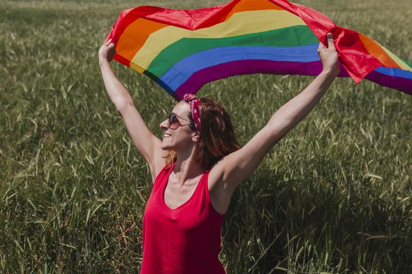 Woman holding the Gay Rainbow Flag on a green meadow outdoors. Happiness, freedom and love concept for same sex couples. LIfestyle outdoors
