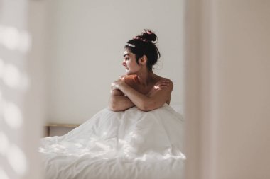  kadın yatakta oturan beyaz çarşaf ile kaplı . Güneş pencereden geliyor. İç yaşam tarzı