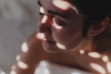  kadın yatakta oturan beyaz çarşaf ile kaplı . Güneş pencereden geliyor. İç yaşam tarzı