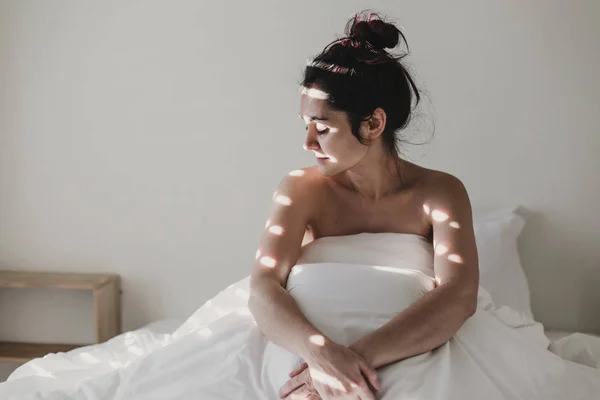 Kvinna Täckt Med Vita Lakan Sittande Sängen Solen Kommer Genom — Stockfoto