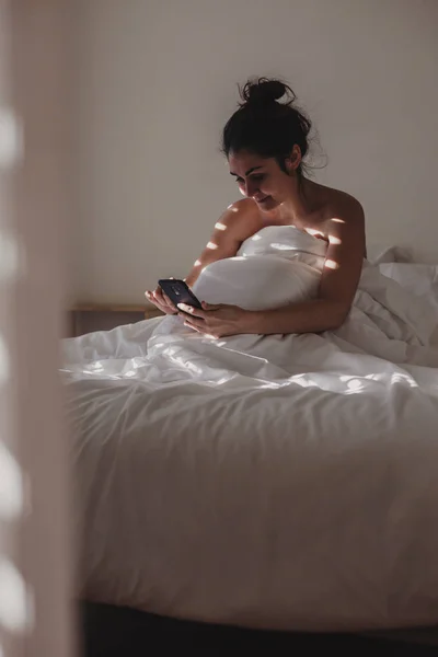 Kvinna Täckt Med Vita Lakan Sittande Sängen Med Telefon Solen — Stockfoto