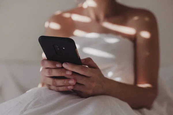 Wanita Ditutupi Dengan Seprai Putih Duduk Tempat Tidur Dengan Telepon — Stok Foto