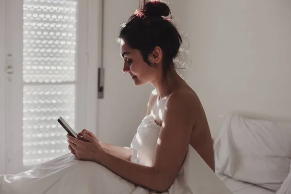 Wanita Ditutupi Dengan Seprai Putih Duduk Tempat Tidur Dengan Telepon — Stok Foto