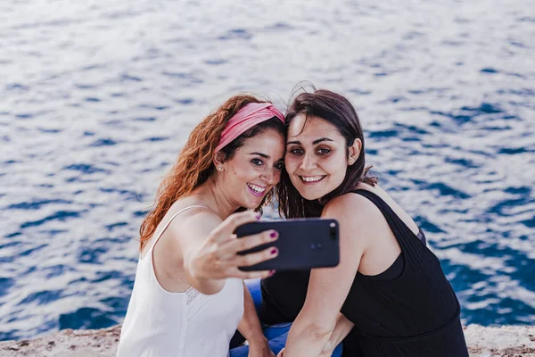 Δύο Γυναίκες Φίλοι Κάθονται Δίπλα Στην Παραλία Χρησιμοποιώντας Κινητό Τηλέφωνο — Φωτογραφία Αρχείου