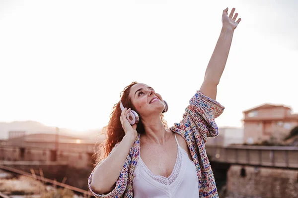 portrait outdoors of a young beautiful woman at sunset listening music on headset and smiling. Lifestyle and music concept