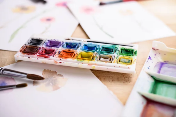 Boya paleti, fırçalar ve suluboya resimler.