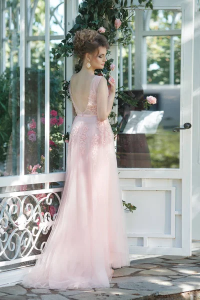 The bride in a long pink dress from the back light on the terrace