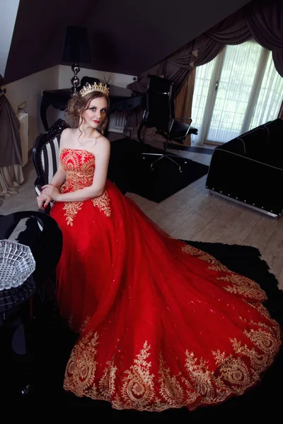 美丽的女人穿着别致的红色礼服和皇冠在别致的内饰 — 图库照片