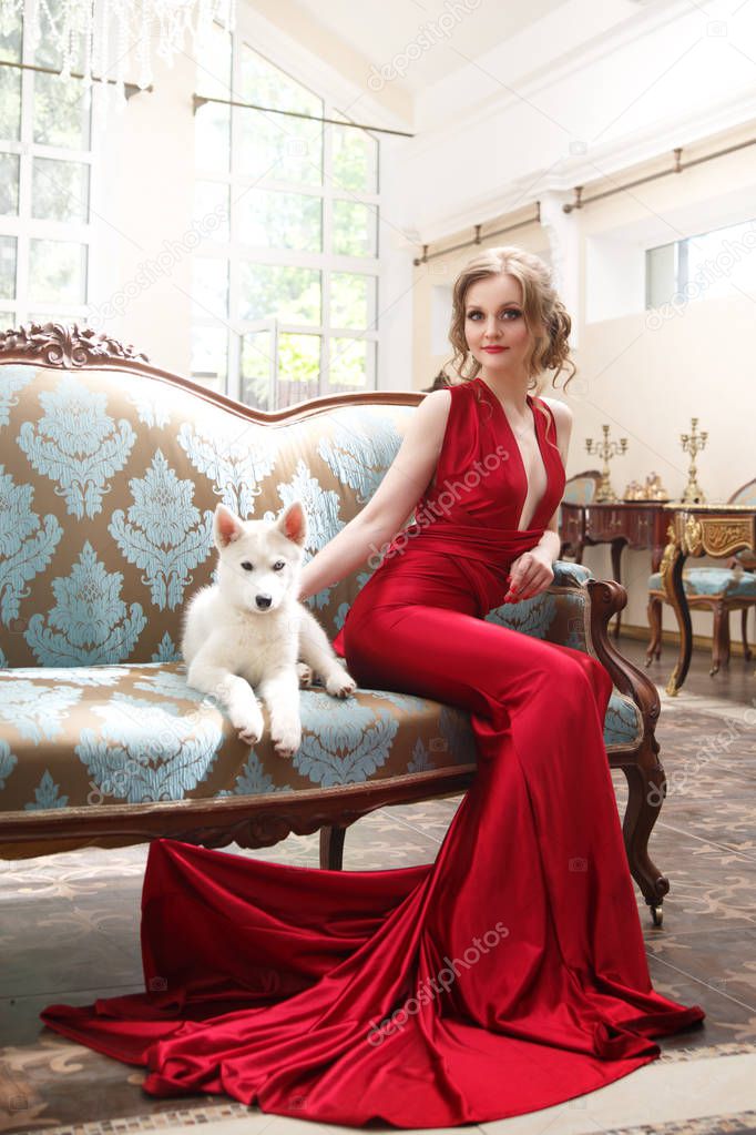 Beautiful woman in an elegant red dress with a cute puppy dogs of the Husky breed in a classic interior.