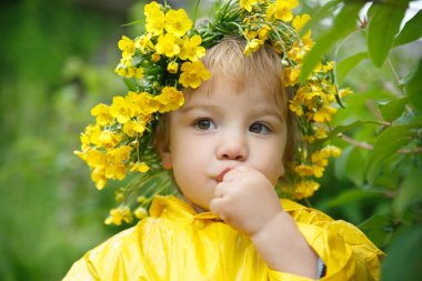 Sarı yağmurluk ve Düğünçiçekleri çelenk içinde küçük bir çocuk bir çalı gelen meyve yer.