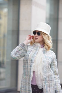Bir güzel şık sarışın kadın palto ve şapka ve güneş gözlüğü üzerinde bir şehir sokak.