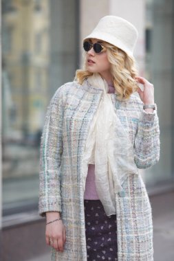 Bir güzel şık sarışın kadın palto ve şapka ve güneş gözlüğü üzerinde bir şehir sokak.