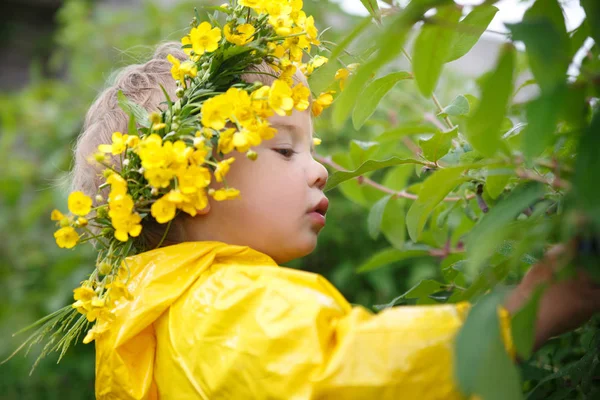 黄色のレインコートとキンポウゲの花輪で小さな子供を食べる ブッシュからの果実 — ストック写真