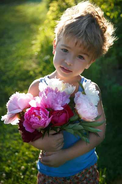 かわいい赤ちゃんが屋外ピンク牡丹の大きな花束を保持しています — ストック写真