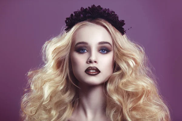 Beauty portrait of a beautiful young blonde woman with gothic make-up and decorative wreath on a purple background.
