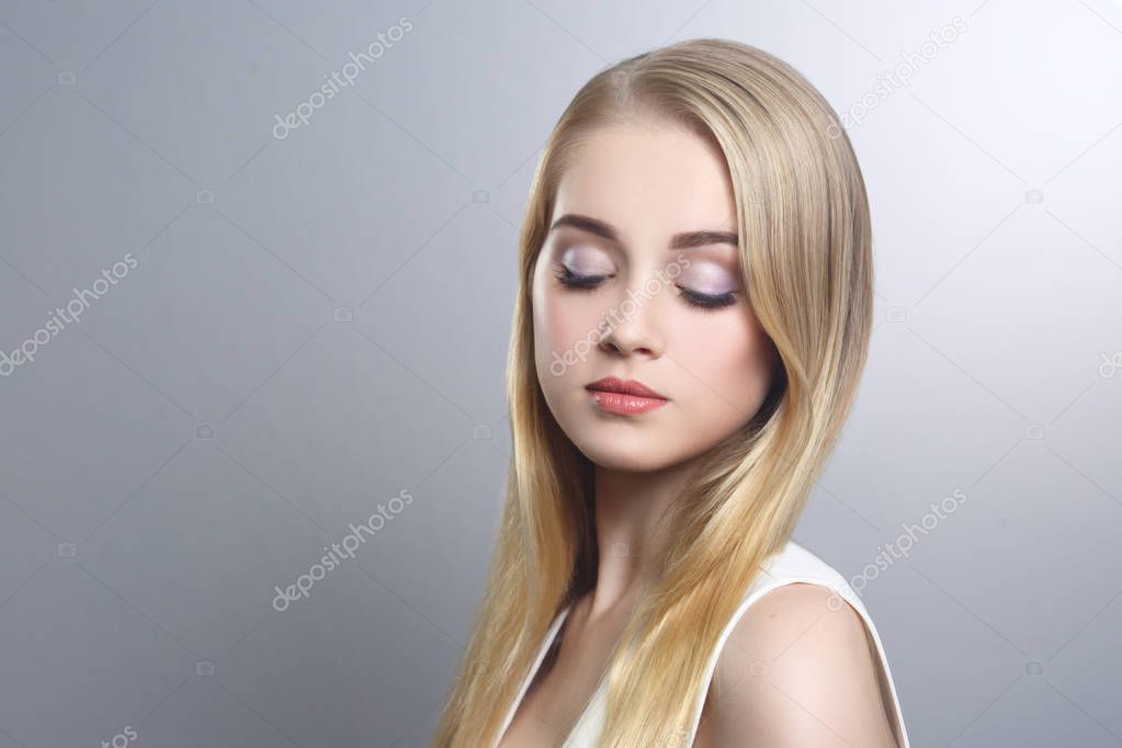 Beauty portrait of a cute blonde with long straight hair isolated groomed on a gray background.