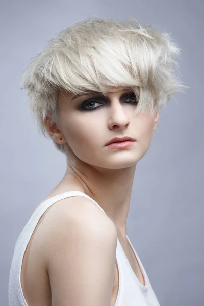 Portrait of blonde woman with stylish short haircut on gray background.